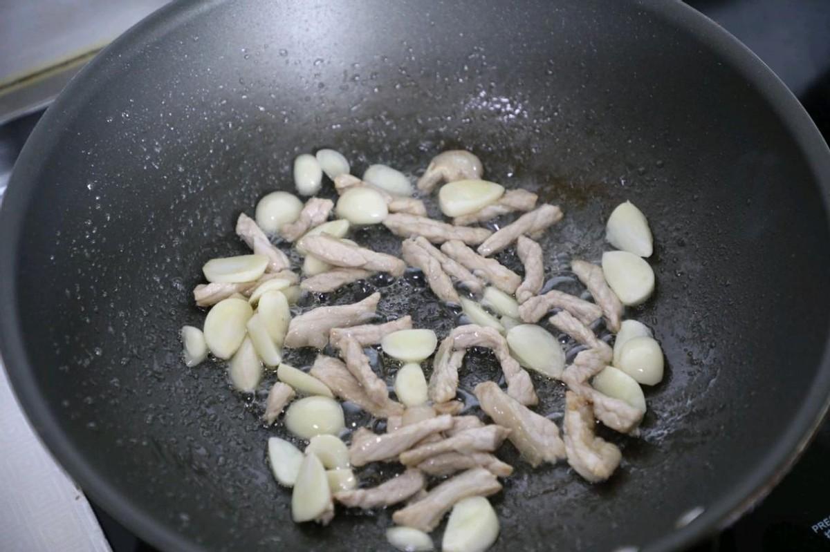 炒锅里面加入少量的花生油，烧热了以后把猪肉丝下进去，把猪肉炒的变色了以后下入蒜片。翻炒出蒜香味。