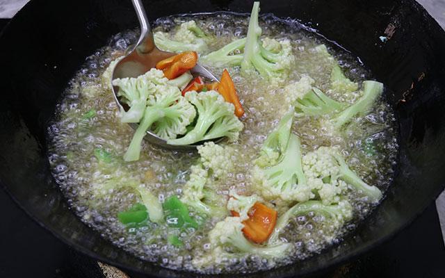 把锅充分烧热加入食用油，油温烧至六成热，下入准备好的花菜和青红椒过一下油，20秒左右，捞出来控干油备用